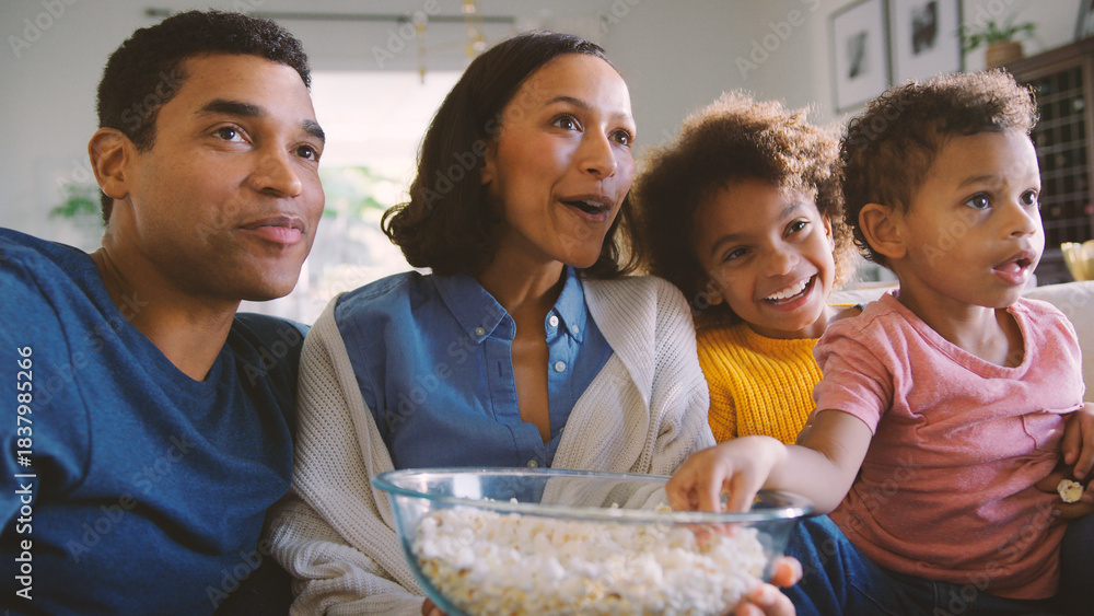 Fototapeta premium Family At Home Sitting On Sofa Watching TV And Eating Popcorn Together