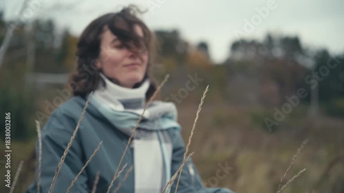 Wind, Hair, Smile: A serene moment of a beautiful Slavic woman in tranquil autumn nature, sitting in tall grass, reflecting on life with a gentle breeze and a soft smile.