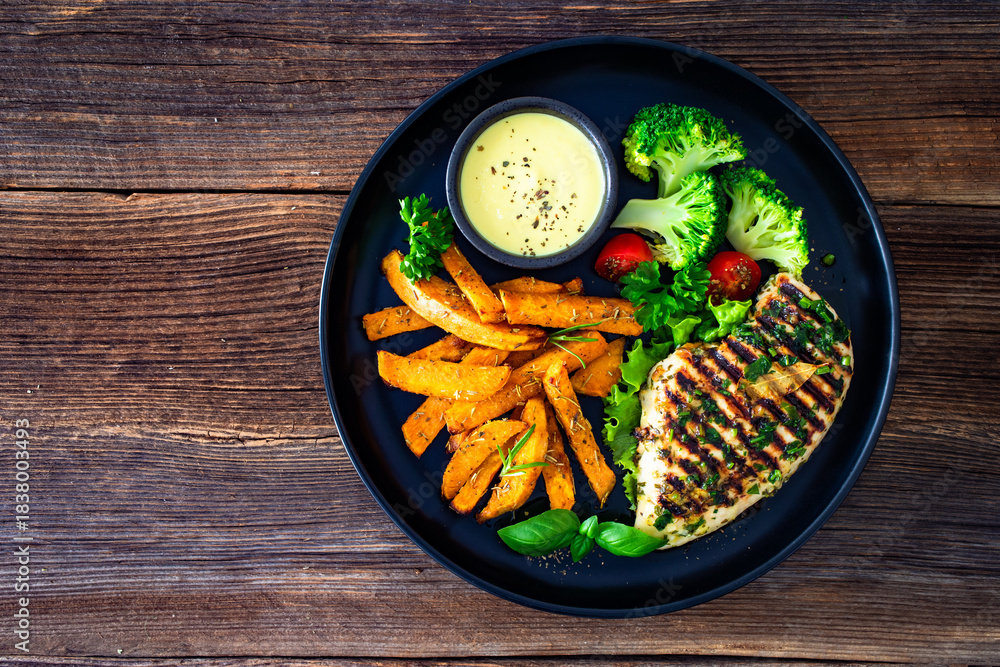 Fototapeta premium Grilled chicken breast, sweet potato fries with barbecue sauce and boiled broccoli on wooden table