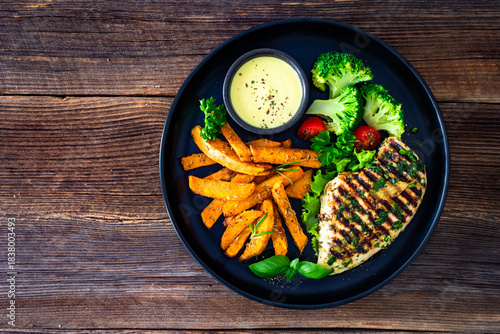 Grilled chicken breast, sweet potato fries with barbecue sauce and boiled broccoli on wooden table
