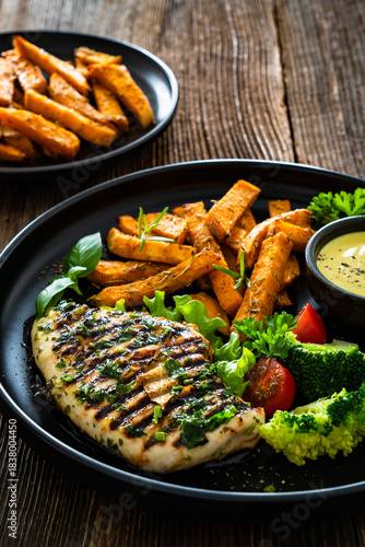 Grilled chicken breast, sweet potato fries with barbecue sauce and boiled broccoli on wooden table
