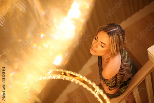 Sexy blond model alluring in bright dress in royal luxury interior with golden chandelier