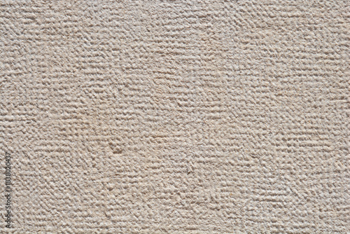 A tight, abstract background shot showing the rough, finely textured surface of a light beige or off-white cut stone wall