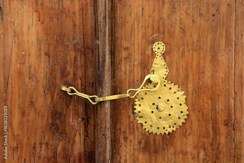 Metal door handle on old brown wooden door. The door handle is painted gold.