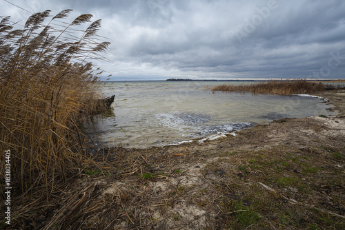 Old rural wooden, fishing boat is moored on the shore of a lake. A gloomy windy day
