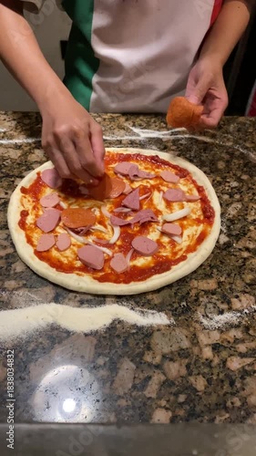 4k vertical video footage of A cook is sprinkling the dough with mozzarella cheese, sausage, peppers and vegetables toppings in pizza restaurant kitchen.