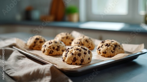 Freshly baked chocolate chip cookies cooling on a baking tray in a bright kitchen.