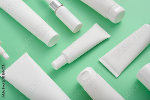 White cosmetic product tubes and bottles arranged on a light green background for skin and hair care