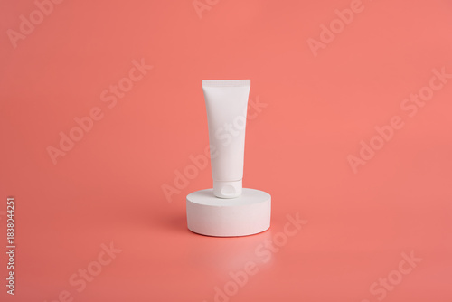 White cosmetic tube placed atop a round platform against a coral background