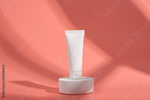 White tube container on a cylinder display stand against a coral colored background