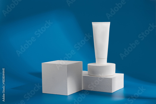 White tube of cosmetic product sits on geometric shapes against blue backdrop