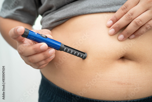 Asian woman injecting herself diabetes injecting insulin in stomach at home.