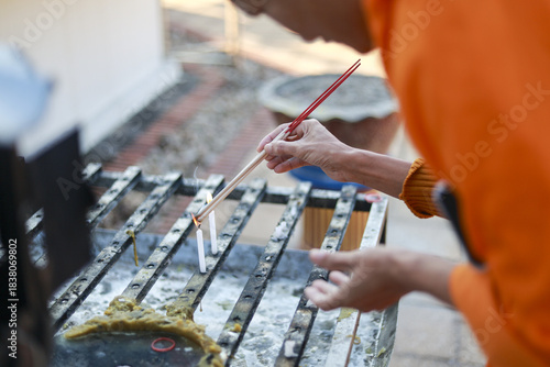 Focused man in orange clothing carefully applying oil to barbecue grill with brush. His concentration shows while he prepares for outdoor summer cooking and grilling