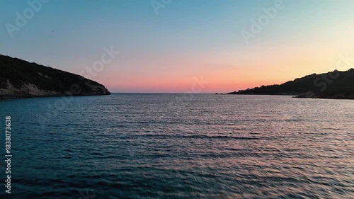 Cinematic Low Aerial Drone Shot Gliding Over Tranquil Turquoise Bay Water Towards a Dramatic Amber and Orange Sunset Sky near Bonifacio, Corsica, France.