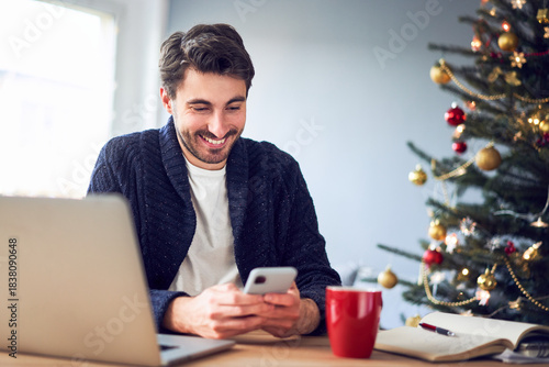 Young man using his phone while working at home office during Christmas season