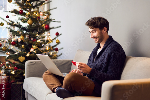 Young man sitting on sofa shopping for Christmas presents online paying with credit card