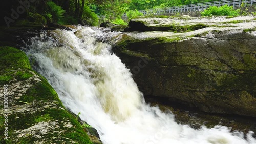 turbulent mountain river flows over mossy rocks. there is a road above with passing traffic nearby. natural sound
