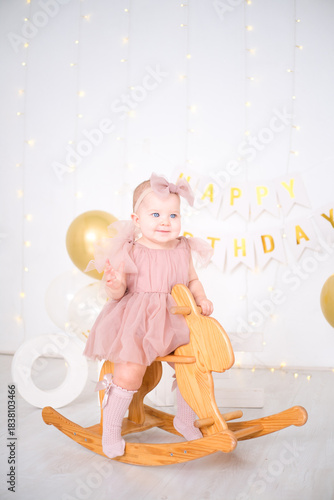 a little blue-eyed girl rides a wooden horse and celebrates her first birthday