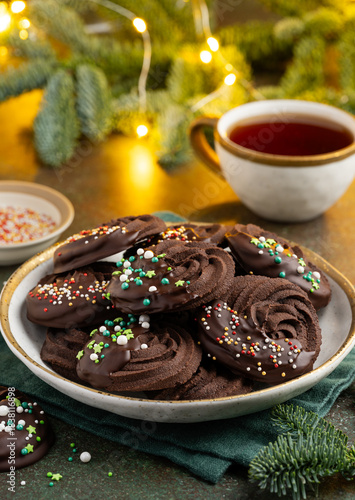 Chocolate Christmas sablé cookies decorated with chocolate and sprinkles on a plate. New Year's festive dessert. Selective focus
