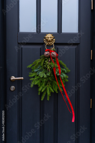 Close-up of a beautiful Christmas wreath with red ribbon and bells on a black door
