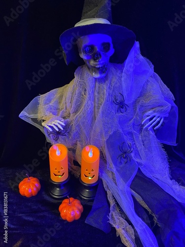 halloween witch with pumpkin. Halloween decoration with two orange LED candles in black holders, small pumpkins, and plastic spiders on a dark background with blue lighting and cobwebs