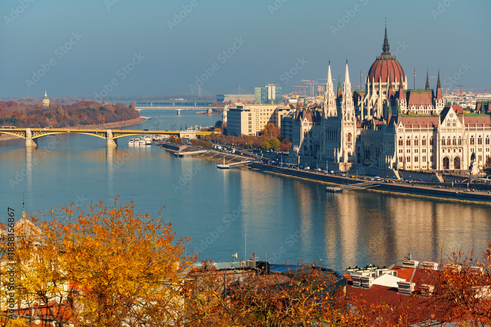 Fototapeta premium Budapest cityscape, panoramic view of city and Danube River, Parliament building with Margit bridge and beautiful architecture in autumn season, trees, branches and yellow leaves in foreground
