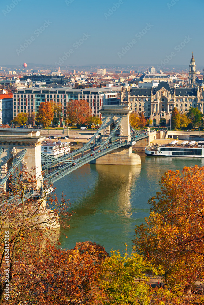 Obraz premium Budapest cityscape, panoramic view of city and Danube River with Chain bridge and beautiful architecture in autumn season, trees, branches and yellow leaves in foreground