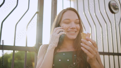 three female friends one disabled woman in a wheelchair enjoys ice cream while talking on her phone outside in the afternoon sunlight near a decorative gate