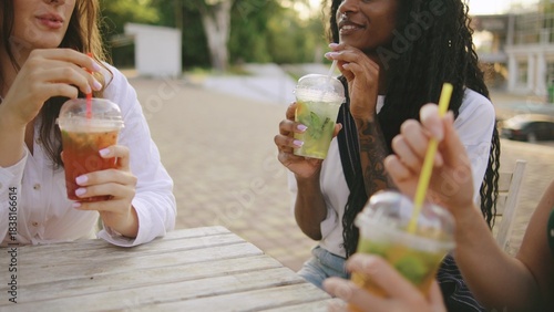 three female multiracial friends one disabled woman in a wheelchair enjoy refreshing drinks outdoors at a sunny gathering near a pool in late afternoon