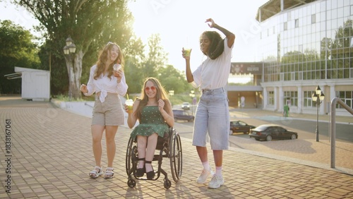 three female multiracial friends one inclusive woman in a wheelchair enjoying drinks and dancing together outdoors at sunset in a vibrant urban setting