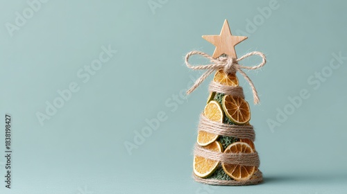 Unique Christmas tree made from dried citrus slices tied with string and topped with a star on a pastel aqua background