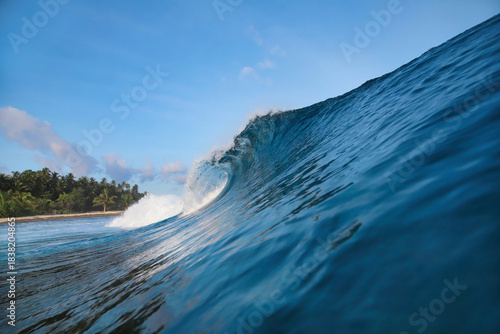Powerful ocean wave curling under sky, palm silhouettes on horizon, translucent turquoise barrel breaking