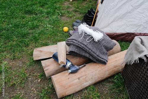 firewood, lighter and hiking accessories on green grass near tent