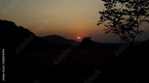 An epic view of a beautiful sunrise over the hills, in front of farmland in rural village