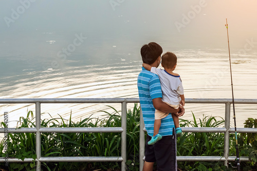 Father with son stand on pier and catching fish on lake background. Family fishing together on pond. Family fishing holiday. Dad with child outdoors near river. Father and boy son fishing together