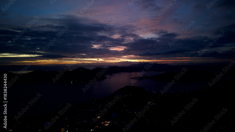 Fototapeta premium High altitude night aerial panoramic view of Coron Bay islands and coastal town lights in Palawan, Philippines, during blue hour twilight under dramatic cloudy sky over calm sea.