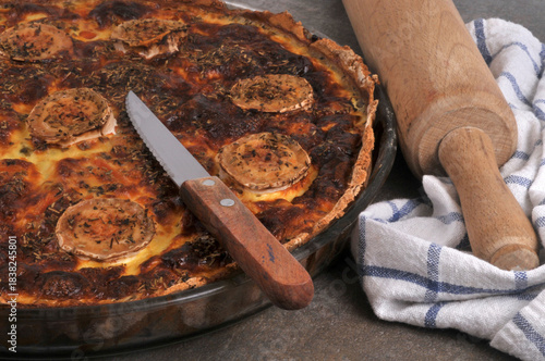 Tarte salée au fromage de chèvre dans un plat avec un couteau en gros plan avec un rouleau à pâtisserie et un torchon