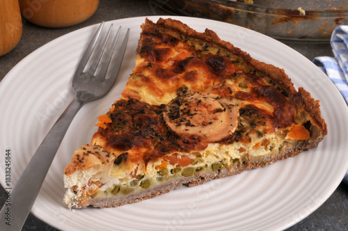 Part de tarte salée au fromage de chèvre et aux légumes dans une assiette avec une fourchette en gros plan