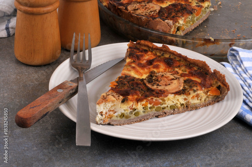Part de tarte salée au fromage de chèvre et aux légumes dans une assiette avec une fourchette et un couteau en gros plan