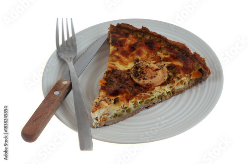 Part de tarte salée au fromage de chèvre et aux légumes dans une assiette avec une fourchette et un couteau en gros plan isolée sur fond blanc