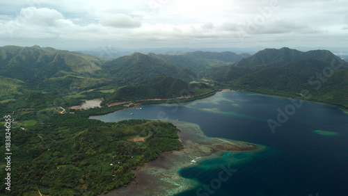 High altitude aerial panoramic view of Sitio Bayang bay and coral reef coastline near Turda in Coron, Palawan, Philippines, with lush green hills under soft overcast natural daylight.