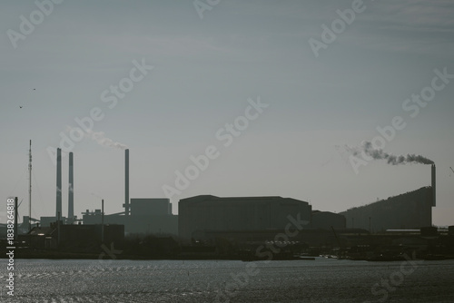 An atmospheric silhouette depicts a sprawling industrial landscape, complete with smokestacks and factories, highlighting the impact of industry on the environment.