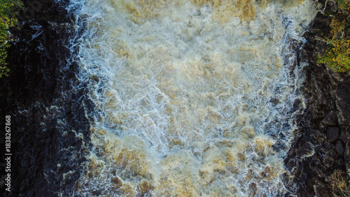 Slika na platnu Aerial view of turbulent waterfall water cascading over dark rock