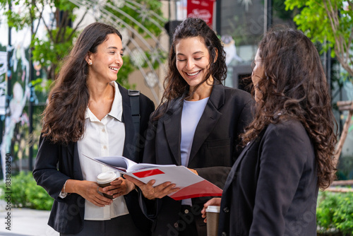 Three businesswomen talking and drinking coffee outdoors, showcasing teamwork, communication, and professional collaboration in a modern corporate environment. Ideal for business, leadership, and work