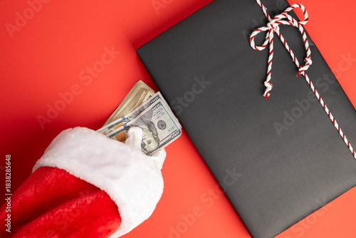 High cost of modern Christmas shopping concept.  Santa hand with a stack of cash over a wrapped present.