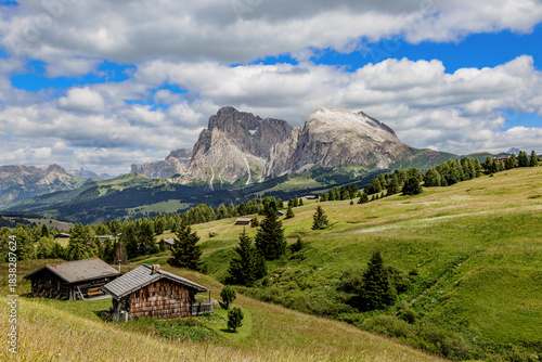 View over the alpine meadows with mountain cabins towards the Langkofel group with the peaks of Langkofel and Plattkofel on the Seiser Alm, Dolomites, South Tyrol, Italy.