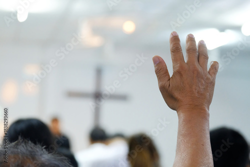 A believer raising a hand in prayer and worship during a church service. The soft focus and added film grain create a classic, emotional atmosphere. Ideal for themes of faith, worship, devotion