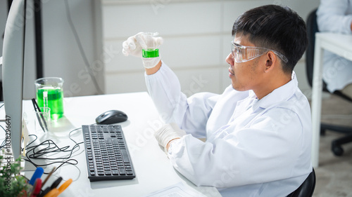 A male scientist examines a green algae solution in a modern laboratory, analyzing concentration and biochemistry for biotechnology or cosmetic research, surrounded by lab equipment and data displays.