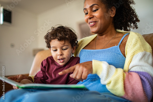 Adult mother reading storybook to young son happily at home