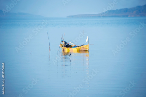 Fototapeta Naklejka Na Ścianę i Meble -  fishing boat and fisherman standing in lake water in foggy weather, golyaka uluabat lake